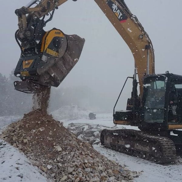Cuchara trituradora MB BF70.2 S4 operando con nieve y escombros.