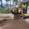 Miniexcavadora CAT con cuchara MB-HDS207 cribando tierra en entorno urbano.