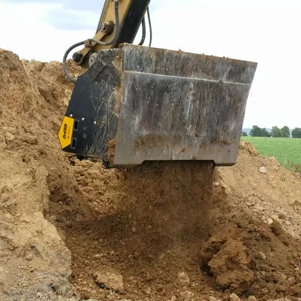 MB-HDS323 de MB Crusher seleccionando tierra húmeda con excavadora sobre campo abierto.