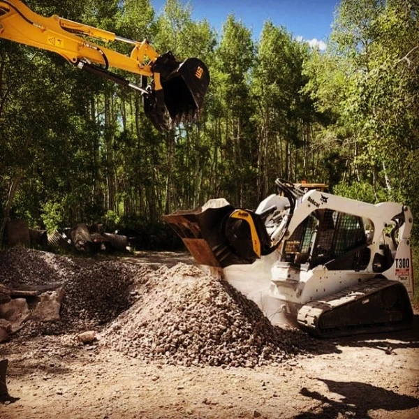 Cuchara trituradora MB L120 S2 triturando escombros con minicargadora Bobcat T300 en obra forestal reduciendo material in situ.