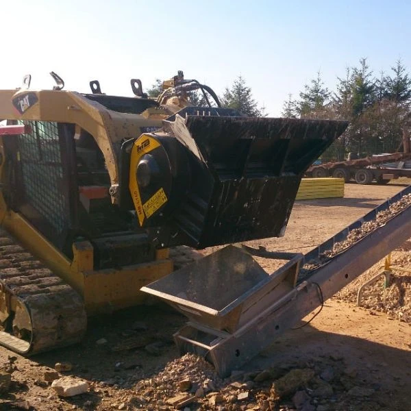 Cuchara trituradora MB-L140 S2 de MB acoplada a minicargadora trabajando en obra.