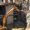 Excavadora JCB con fresadora MB-R800 demoliendo muro vertical de hormigón armado en obra urbana.
