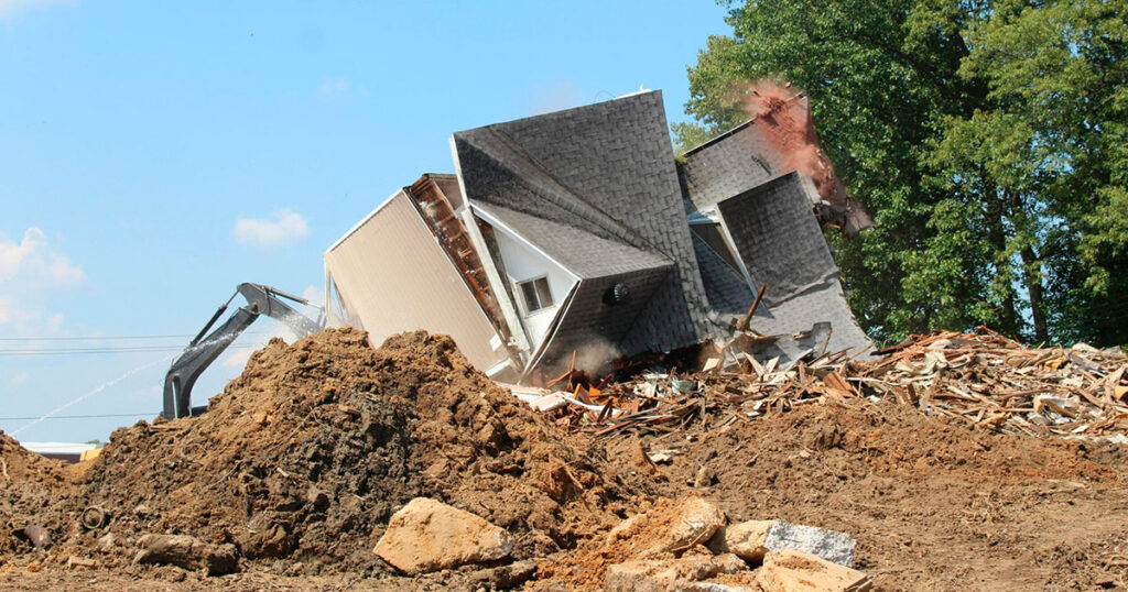 Casa en proceso de demolición controlada con maquinaria especializada, destacando la seguridad y sostenibilidad en el Día Internacional de la Demolición.
