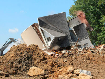 Casa en proceso de demolición controlada con maquinaria especializada, destacando la seguridad y sostenibilidad en el Día Internacional de la Demolición.
