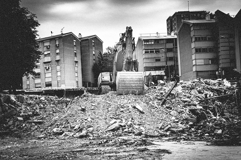 Excavadora realizando demolición segura en zona urbana con escombros en primer plano durante el Día Internacional de la Demolición.