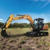 Excavadora SANY SY95C en acción trabajando en campo abierto con brazo hidráulico extendido y orugas sobre terreno natural.