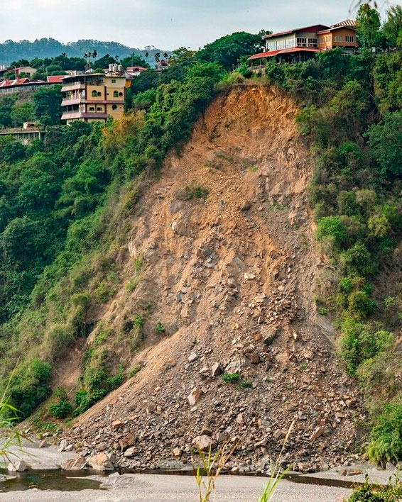 Desprendimiento de tierra en ladera con viviendas en riesgo donde equipos para derrumbes de Protección Civil son necesarios.