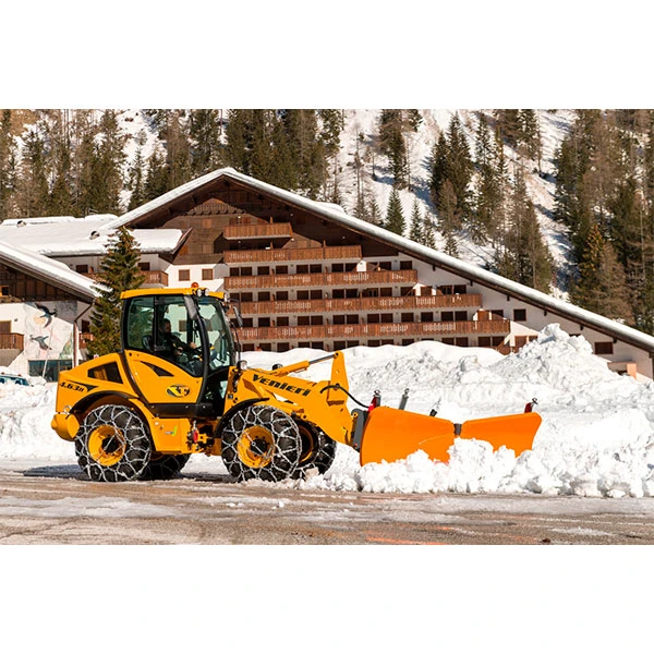 Pala cargadora Venieri 4.63 H equipada con cadenas para nieve y cuchilla quitanieves trabajando frente a un complejo hotelero de montaña nevado.